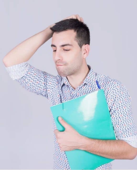 Jeune homme perplexe, une main sur la tête, serrant une chemise cartonnée verte contre lui