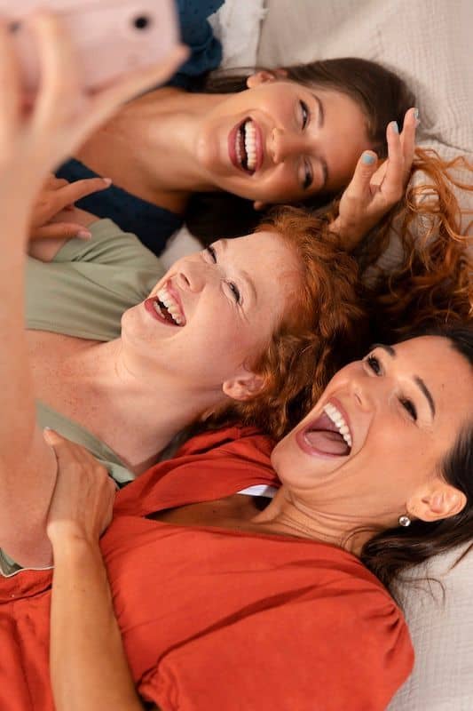 Trois femmes allongées côte à côte, riant aux éclats
